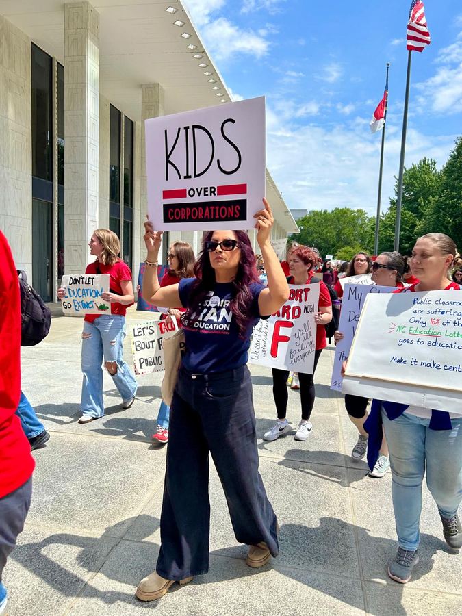 Dr. Samira Khan at a public education rally holding a sign reading Kids Over Corporations