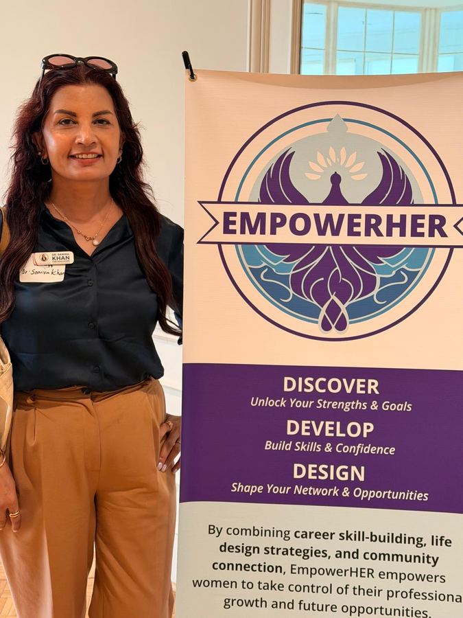 Dr. Samira Khan beside an EmpowerHER banner at a women's professional development event